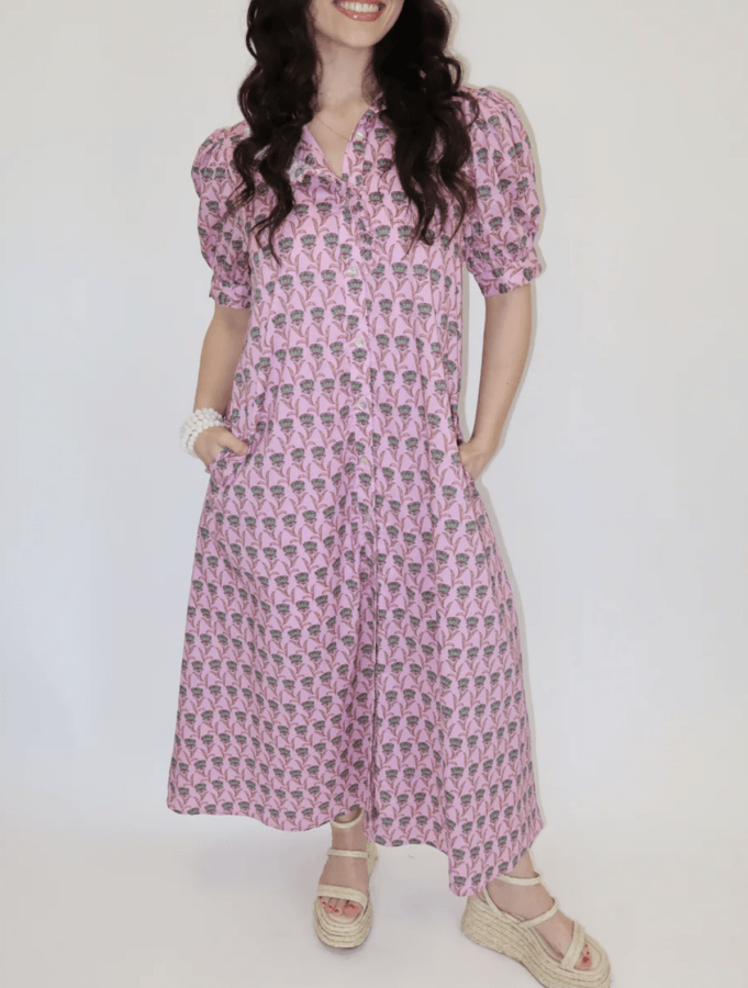 19 Fresh FINDS Around BHAM: Closet Refreshers, Entertaining Picks & More - 10 Woman wearing a pink patterned button-down dress with puff sleeves, hands in pockets, paired with beige wedge sandals and a white bracelet, standing against a plain background.