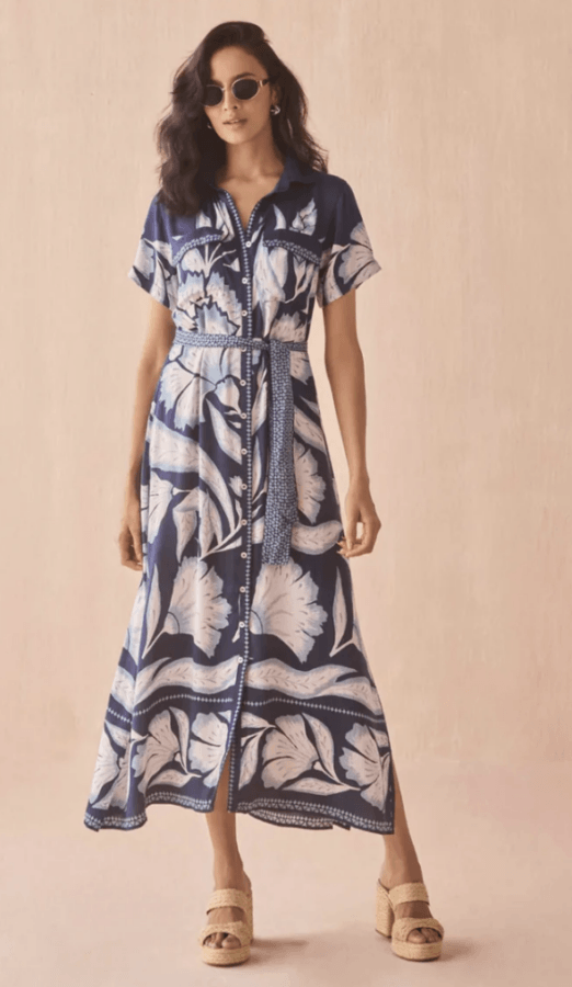 19 Fresh FINDS Around BHAM: Closet Refreshers, Entertaining Picks & More - 5 Woman wearing a blue and white floral button-down maxi dress with a belt, sunglasses, and beige wedge sandals, standing against a light pink background.