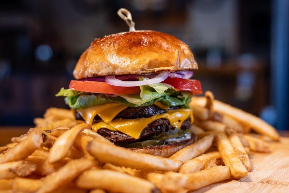A must-try double cheeseburger with lettuce, tomato, onion, and pickles on a bun, served with French fries from Back Forty.
