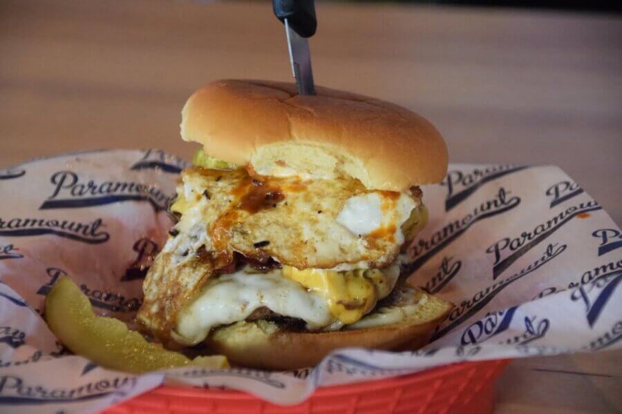 11 Must-Try Burgers in Birmingham - 12 A BHAM cheeseburger topped with a fried egg and sauce, served in a red basket with a sliced pickle and branded paper; a knife is inserted into the burger at Paramount.