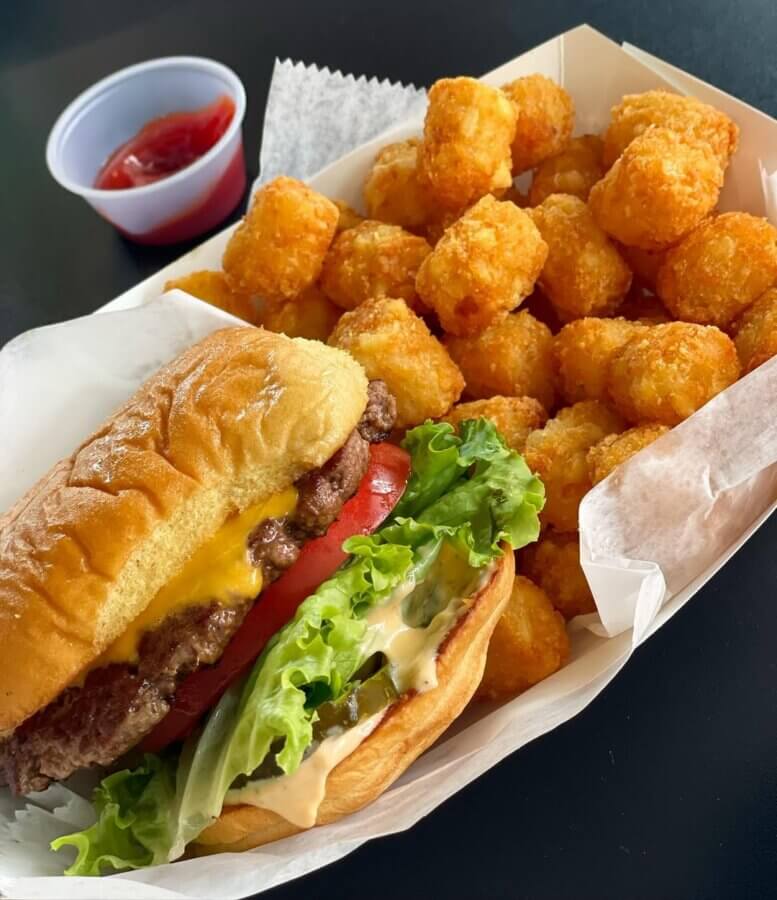 11 Must-Try Burgers in Birmingham - 7 A must-try BHAM classic: a cheeseburger with lettuce, tomato, and sauce in a bun, served with crispy tater tots and ketchup in a small cup at The Standard.