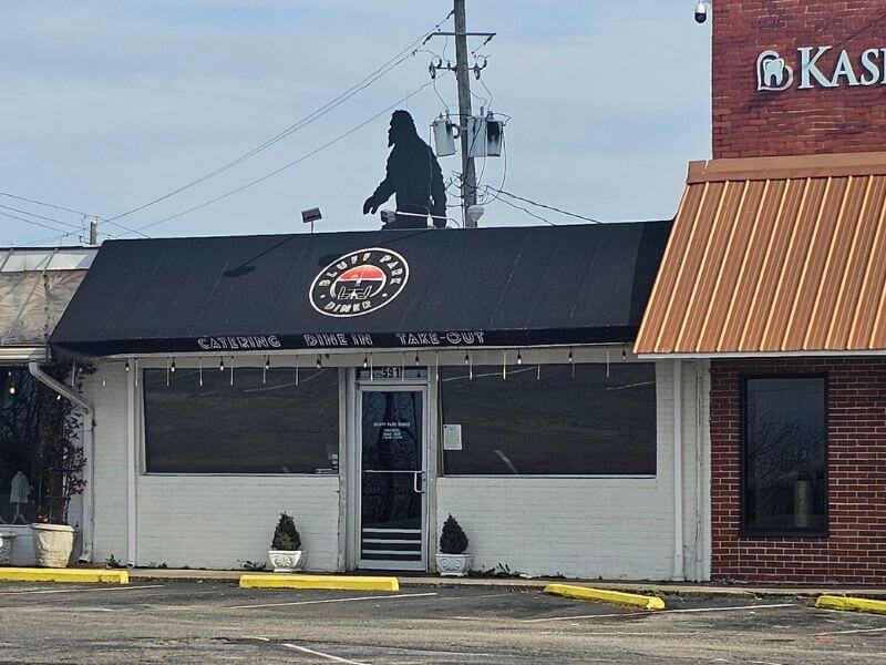 Your Guide to BHAM's Bluff Park - 5 The Bluff Park Diner with a black awning displaying its logo and the words "Catering Dine In Take Out," featuring a large Bigfoot silhouette on the roof—a quirky spot often highlighted in any Bluff Park guide.