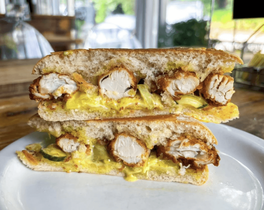 10 New Birmingham Restaurants to Try This Month - 2 Halved fried chicken sandwich with melted cheese and pickles on toasted bread, served on a white plate.