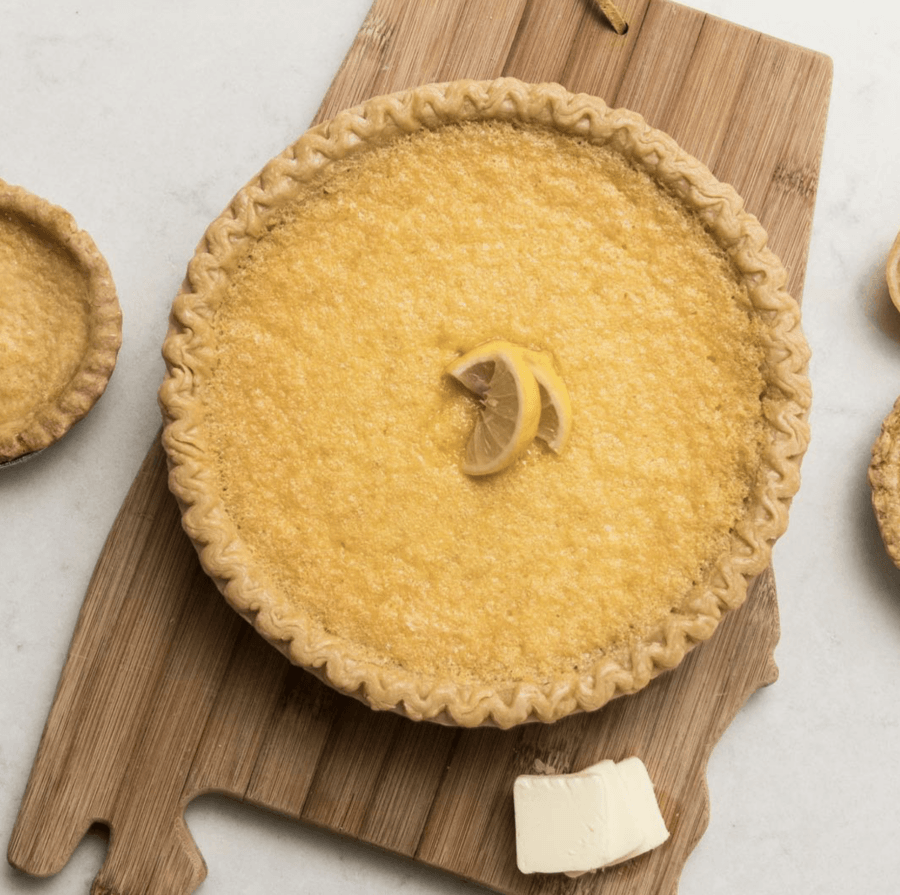 10 New Birmingham Restaurants to Try This Month - 3 A whole lemon pie with a crimped crust sits on a wooden board, garnished with lemon slices; a pat of butter and a small pie are nearby.