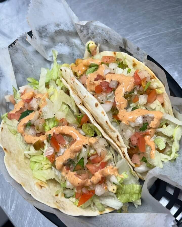 10 New Birmingham Restaurants to Try This Month - 8 Two soft shell tacos filled with shredded lettuce, diced tomatoes, onions, and drizzled with a creamy orange sauce—served on parchment in a black basket. A must-try at one of the best new restaurants in Birmingham!.