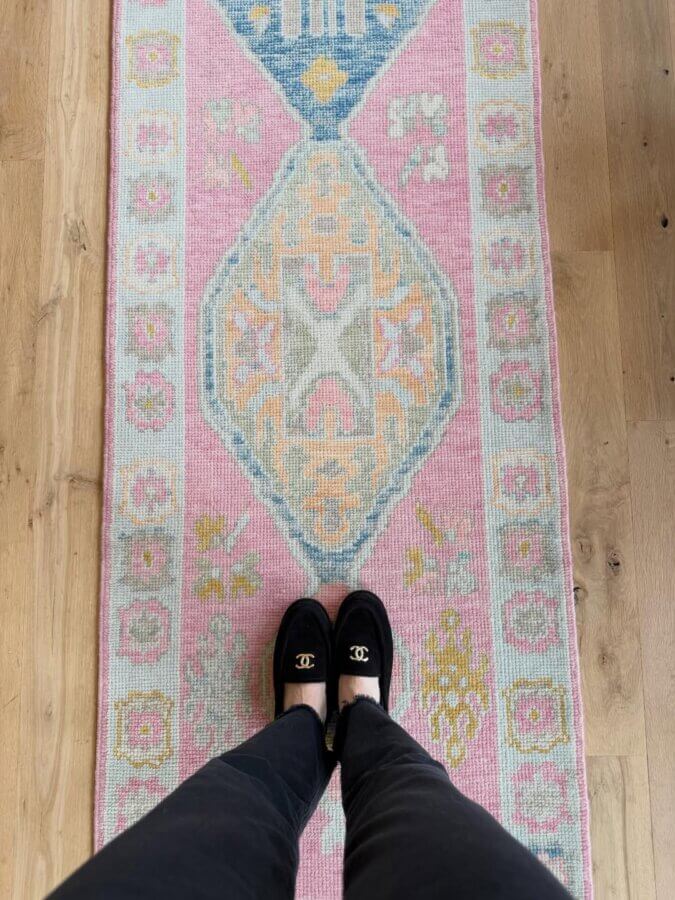 10 New Retail Spots to Check Out in BHAM (+1 Coming Soon!) - 13 Person wearing black Chanel loafers and black pants standing on a colorful, patterned pink and pastel area rug placed on a light wood floor at LillieKat Rugs.