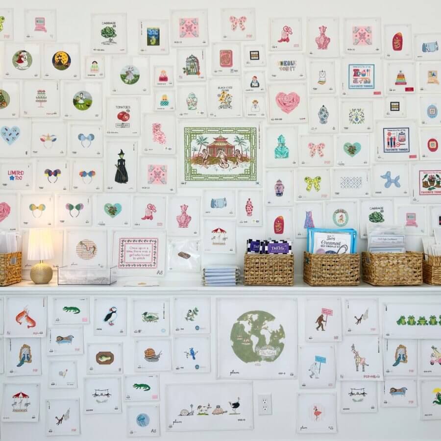 10 New Retail Spots to Check Out in BHAM (+1 Coming Soon!) - 3 A wall covered at The Southern Stitch Needlepoint with neatly arranged small art prints and illustrations above a white counter holding baskets and stacks of paper or cards.