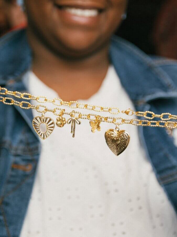 She’s Behind a BHAM Charm Bar, Craft Club, AND a Book Bus! - 8 A person holds up gold chain necklaces from the Charm Bar, featuring various charms like a heart, butterfly, cross, and flower.