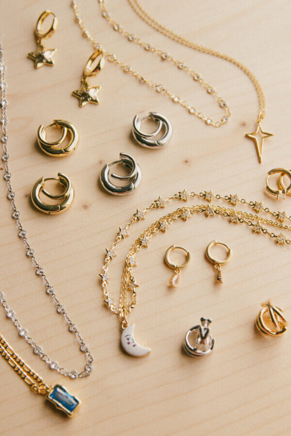 She’s Behind a BHAM Charm Bar, Craft Club, AND a Book Bus! - 3 Assorted gold and silver jewelry from the Craft Club Charm Bar, including necklaces, hoop earrings, and pendants, arranged on a light wooden surface in BHAM.