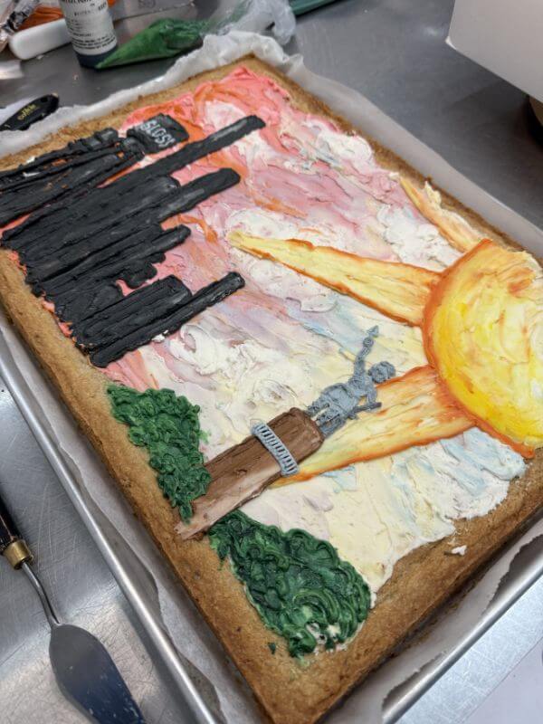 The Baker Everyone in Bluff Park Is Talking About - 5 Rectangular cookie cake by Good Neighbor Baking, decorated with colorful icing depicting a city skyline, sun, trees, and the Vulcan statue against a sunset sky.