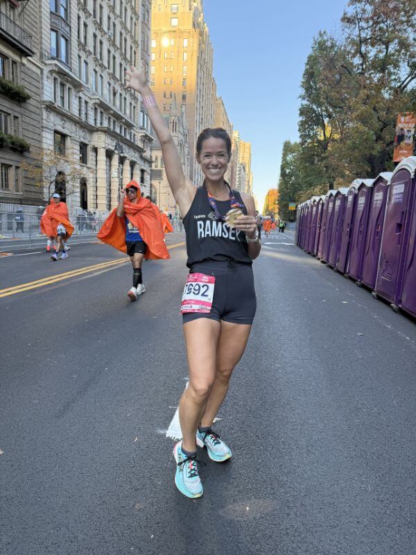 The Baker Everyone in Bluff Park Is Talking About - 8 Ramsey Nuss wearing a race bib and medal stands on a city street, smiling and raising one arm. Portable toilets and other runners are in the background.