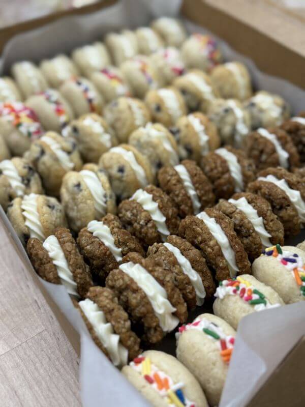 The Baker Everyone in Bluff Park Is Talking About - 4 A box filled with assorted cookie sandwiches from Good Neighbor Baking, some with sprinkles, some with chocolate chips, and others made with oatmeal cookies—all crafted by Ramsey Nuss and filled with white cream.