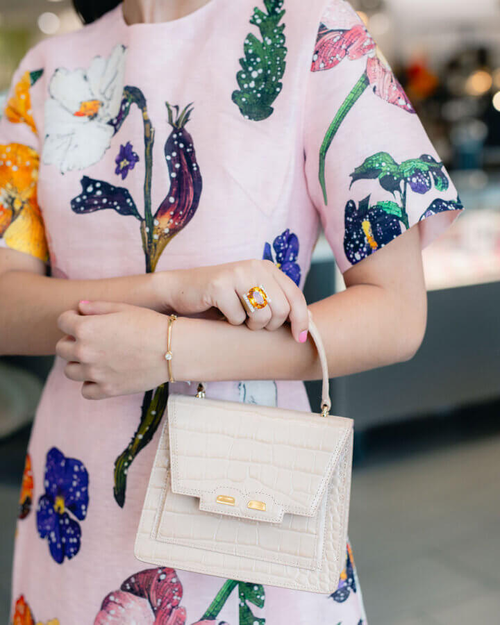 3 BHAM Boutiques Share Their Favorite Spring 2026 Looks - 8 A person in a floral dress holds a small beige handbag, wearing a large yellow gemstone ring and a delicate bracelet.
