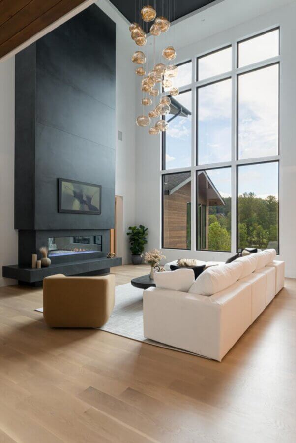 Why the South's Top Home Builders Use C3 Studio - 5 Modern living room with large windows, a white sectional sofa, tan armchair, minimalist fireplace, and a cluster pendant light fixture—showcasing the elegance possible with expert custom home design services.