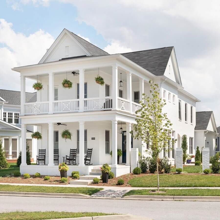 Why the South's Top Home Builders Use C3 Studio - 3 Two-story white house with black shutters, double front porches, rocking chairs, and hanging ferns showcases custom home design services and a landscaped yard on a sunny day.