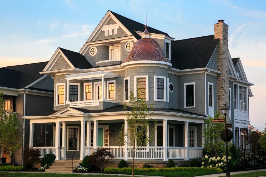 Why the South's Top Home Builders Use C3 Studio - 2 A large, two-story Victorian-style house with gray siding, white trim, a rounded turret, wraparound porch, and landscaped front yard at sunset—perfectly showcasing custom home design services.