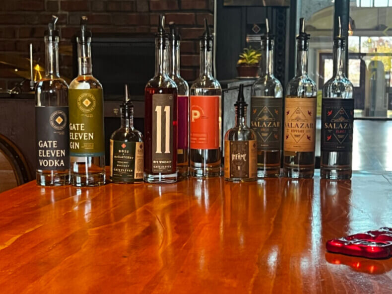 Your Guide to Chattanooga's Culinary Scene - 5 A row of various liquor bottles, including vodka, gin, whiskey, and others, are lined up on a wooden table in a dimly lit room with brick and wood accents—perfect inspiration if you're searching for where to eat in Chattanooga.