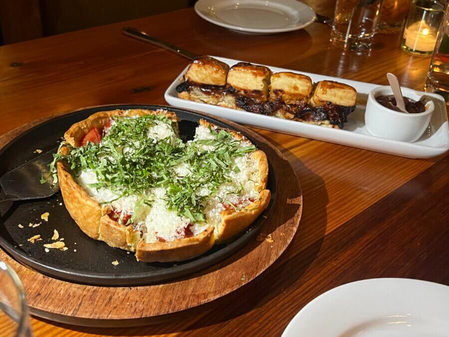 Your Guide to Chattanooga's Culinary Scene - 4 A deep-dish pizza topped with cheese and herbs on a pan, next to a plate of pastries with a small bowl of sauce, served on a wooden table in Chattanooga.