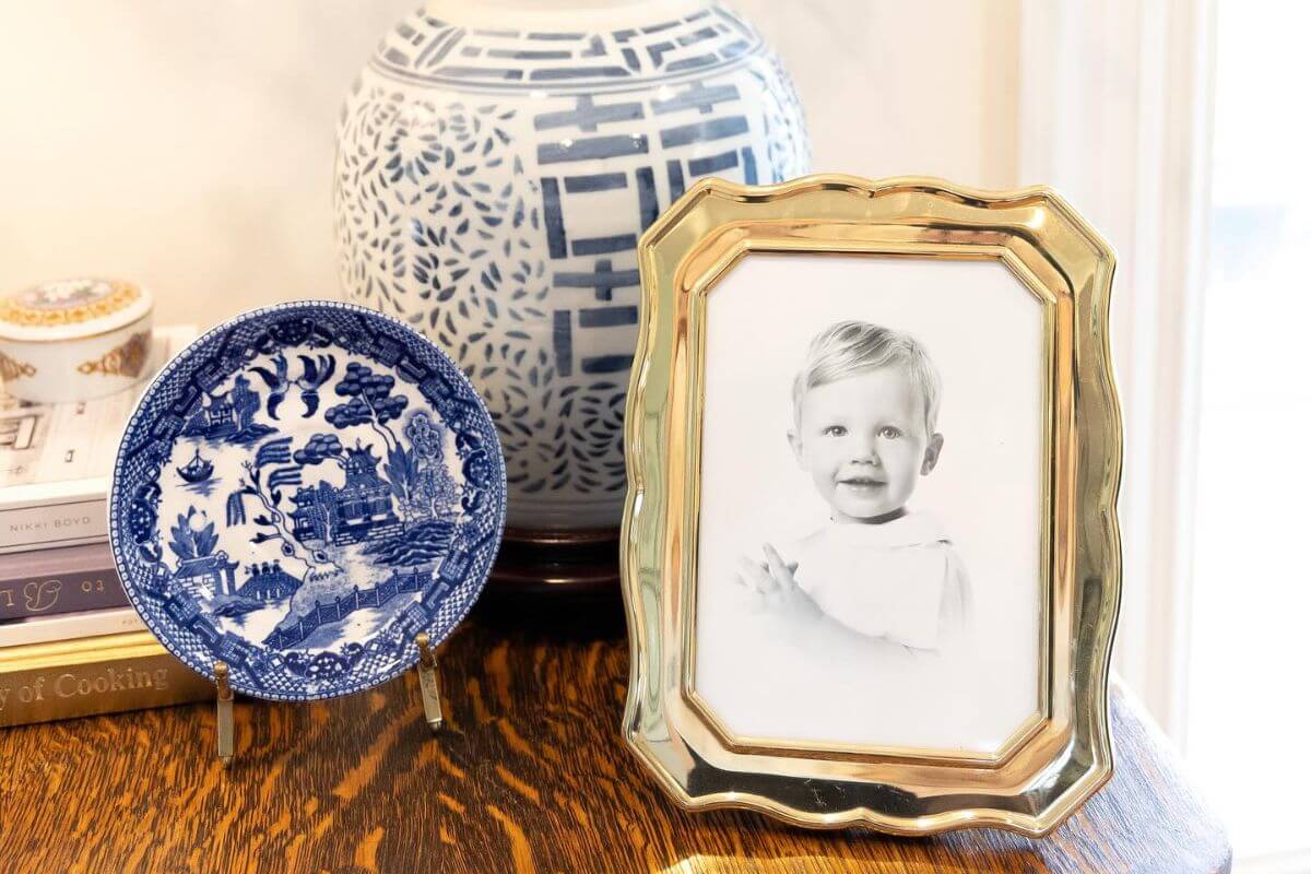 A framed black-and-white photo by Southern heirloom portrait photographers sits on a wooden table next to a blue and white decorative plate and a patterned ceramic vase.