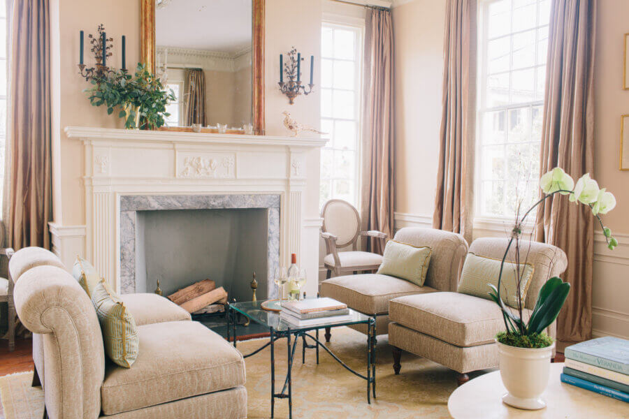 6 Striking Southern Hotels Designed by Top Talent - 16 Elegant hotel living area with beige upholstered furniture, a glass coffee table, potted orchid, and a decorative white fireplace with a large mirror and wall sconces—exuding stylish interior design.