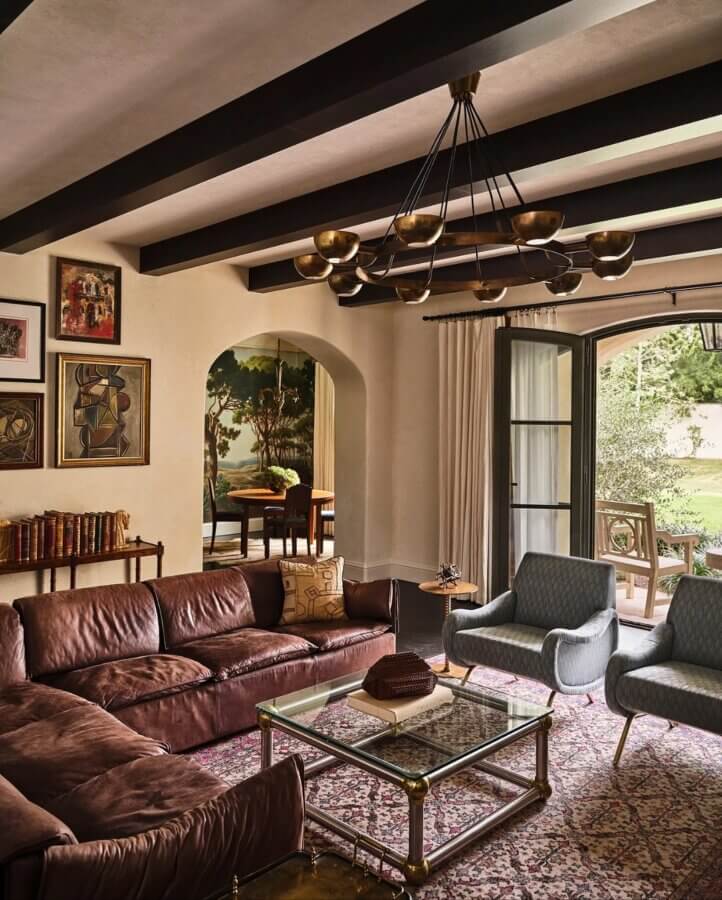 6 Striking Southern Hotels Designed by Top Talent - 15 A lounge area in one of the most beautiful hotels, featuring a brown leather sectional sofa, two gray armchairs, a glass coffee table, and wall art, seamlessly connecting to the dining area and outdoor patio.