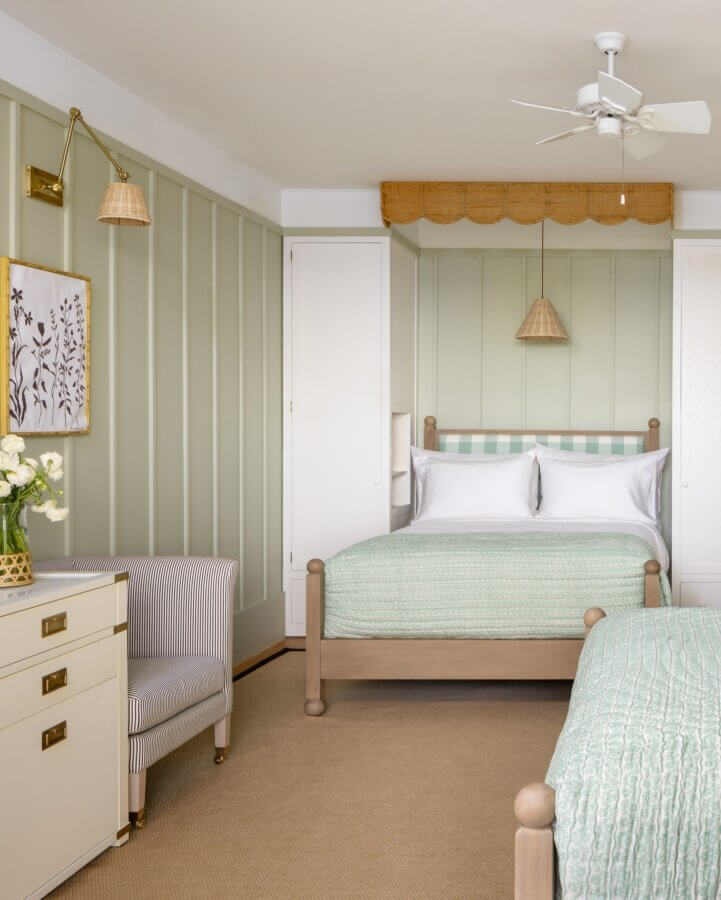 6 Striking Southern Hotels Designed by Top Talent - 9 A neatly arranged bedroom with twin beds, light green panel walls, a striped chair, a ceiling fan, and decorative wall lights.
