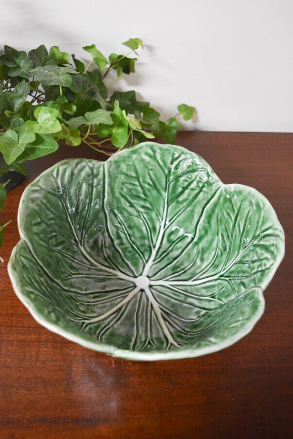 18 Nashville FINDS We're Loving This Month - 15 A ceramic bowl shaped and painted to resemble a green cabbage leaf, featured in the FINDS Draft for March 2026, sits on a wooden surface with leafy green plants in the background.