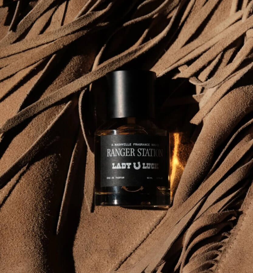 18 Nashville FINDS We're Loving This Month - 12 A bottle of Ranger Station Lady Luck perfume rests on brown suede material with fringe detailing, capturing those unique FINDS Draft moments for March 2026.