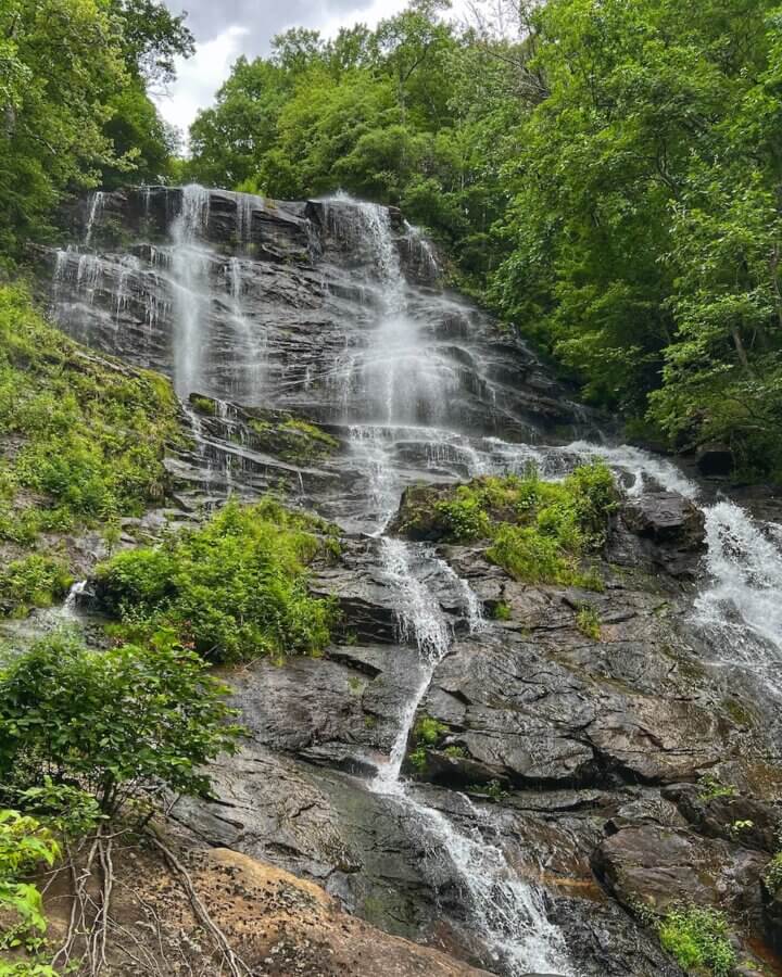 How to Eat, Shop & Explore Your Way Through Georgia - 15 A tall waterfall cascades down dark, rocky tiers surrounded by lush green trees and vegetation under a cloudy sky—one of the breathtaking things to do in Georgia for nature lovers.