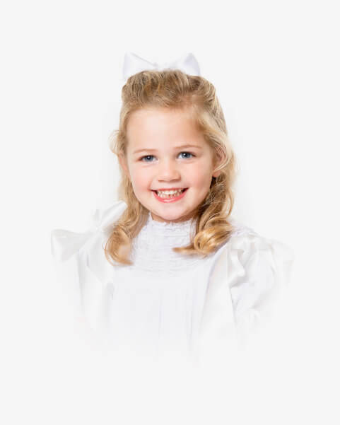 Heirloom Portraits Are Making a Comeback! - 7 Young girl with blonde hair, wearing a white dress and a white bow, smiling at the camera against a white background—capturing the timeless style cherished by Southern Heirloom Portrait Photographers.