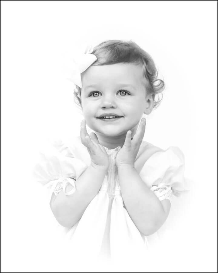Heirloom Portraits Are Making a Comeback! - 5 A young child with short curly hair and a bow, wearing a light dress, smiles and holds their hands near their face against a white background—capturing the timeless style of Southern heirloom portrait photographers.