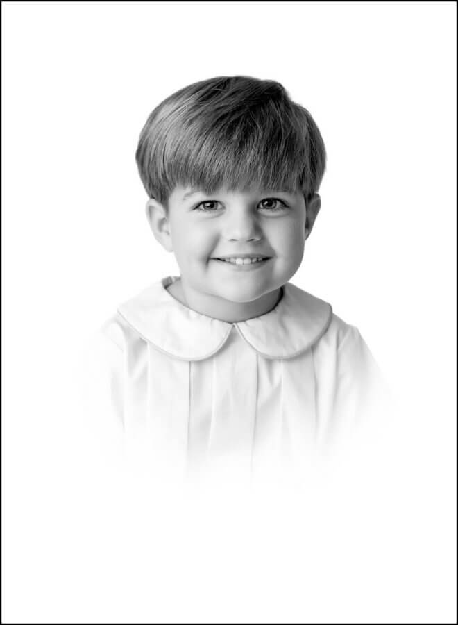 Heirloom Portraits Are Making a Comeback! - 4 Black and white portrait of a young child with light hair, smiling in a collared shirt, captured in the timeless style favored by Southern heirloom portrait photographers, against a plain white background.