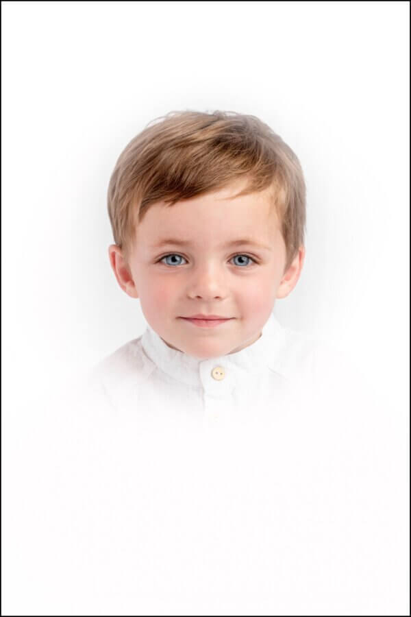 Heirloom Portraits Are Making a Comeback! - 8 A young child with light brown hair, blue eyes, and a white button-up shirt, photographed against a white background in the timeless style favored by Southern heirloom portrait photographers.