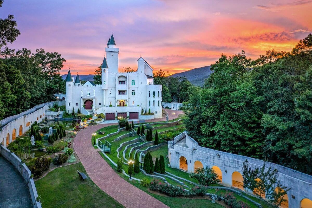 White castle-like building with towers surrounded by trees and gardens at sunset, with a pathway leading through landscaped grounds—one of the South’s hidden gems perfect for travel enthusiasts.