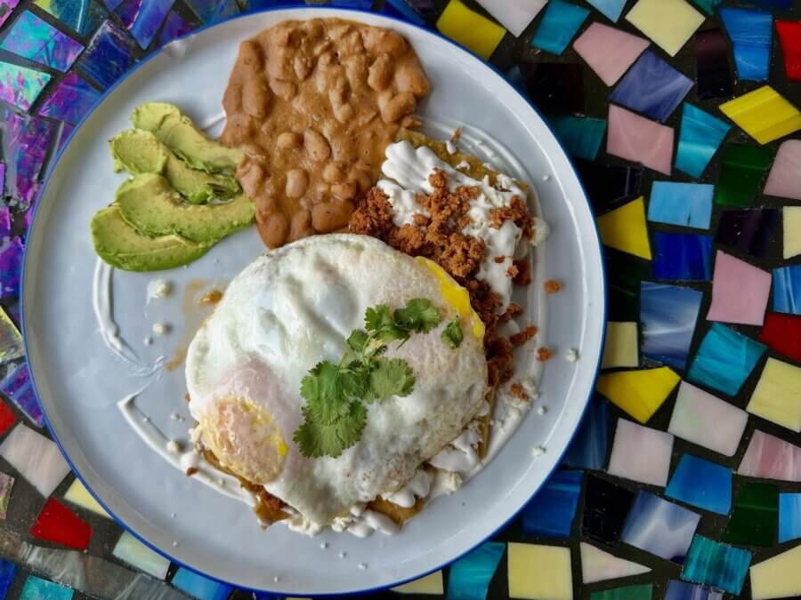 The Best Brunches in Louisville: 13 Must-Try Spots - 6 A plate with avocado slices, refried beans, chorizo, and huevos rancheros topped with sour cream and cilantro, served on a colorful mosaic table—perfect for anyone seeking the Best Brunch Louisville has to offer.