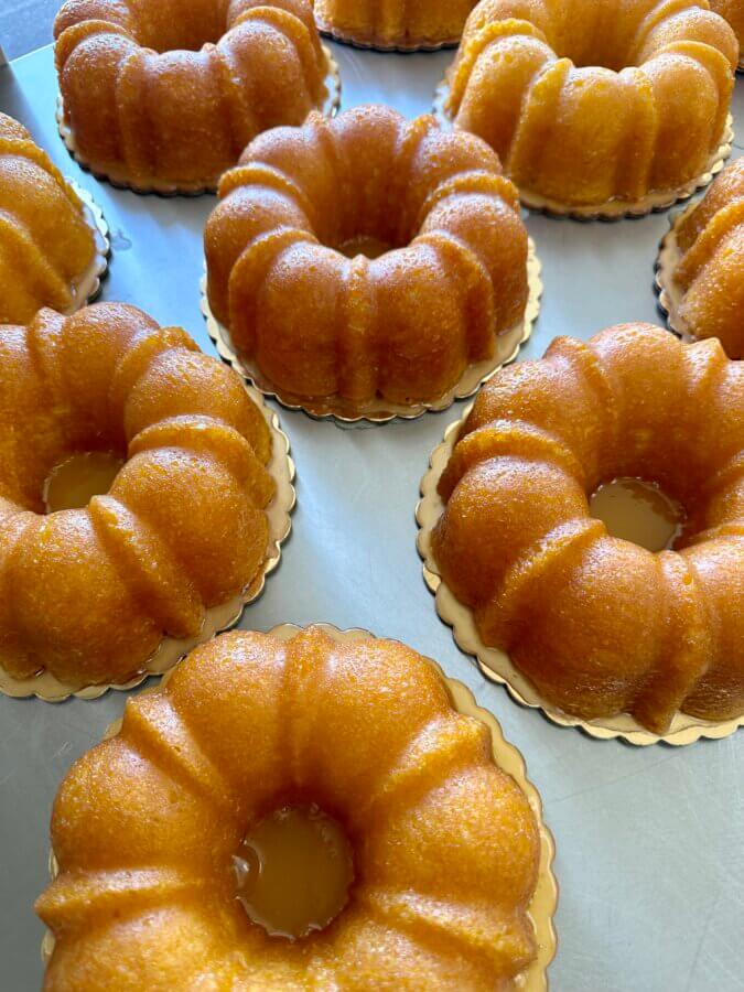 Meet the Sisters Behind Louisville’s SissyCakes Bakery - 4 Several small, golden SissyCakes bundt cakes are arranged closely together on a light-colored surface, each sitting on a round gold paper base and topped with Signature Glaze — a delightful treat from Louisville.