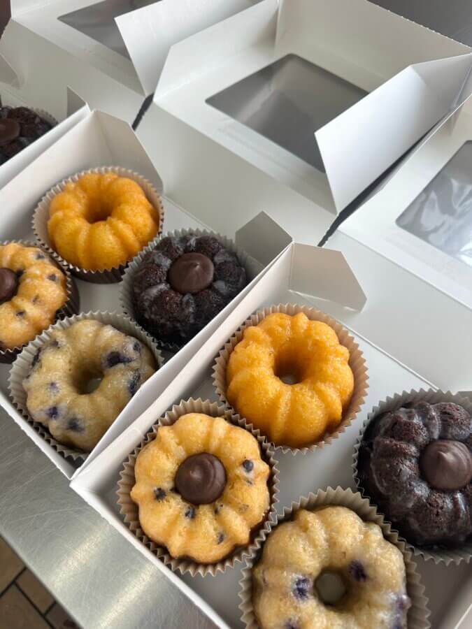 Meet the Sisters Behind Louisville’s SissyCakes Bakery - 3 Three white boxes from SissyCakes each contain four mini bundt cakes in different flavors, like chocolate with chocolate centers, blueberry, and yellow cake—arranged in paper liners and topped with signature glaze.