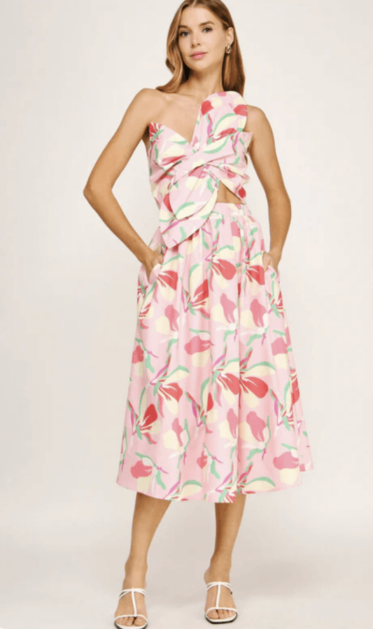 16 Louisville FINDS for April: Spring Style, Derby-Ready Decor & Must-Have Gifts - 5 Woman wearing a pink, floral-patterned, sleeveless dress with a twisted bodice and midi skirt—perfect for spring events or discovering local finds in Louisville—stands in white heeled sandals against a plain backdrop.