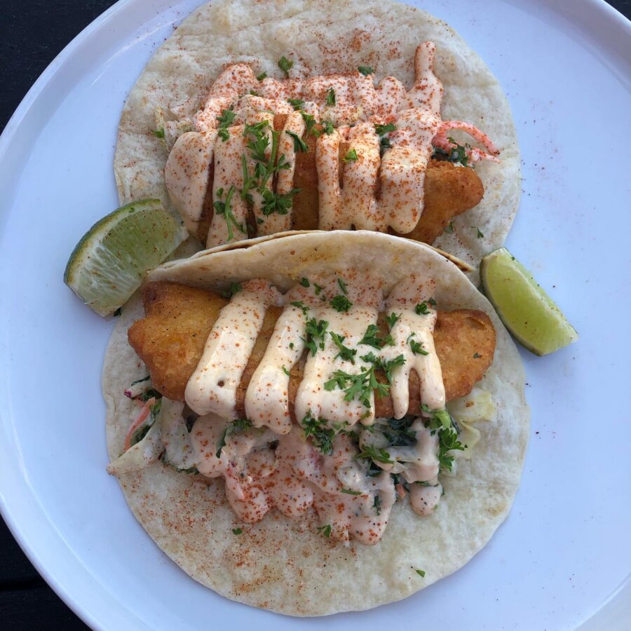 4 New Louisville Restaurants (+2 New Menus!) to Try This Month - 2 Two fish tacos with creamy sauce, chopped herbs, and lime wedges on a white plate.