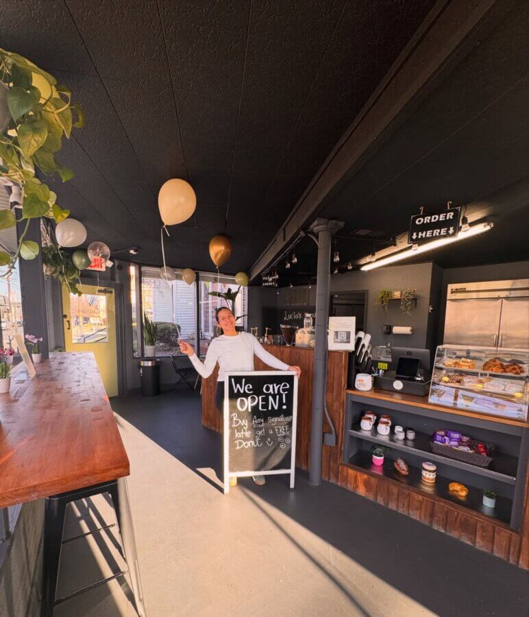 4 New Louisville Restaurants (+2 New Menus!) to Try This Month - 4 Person holding balloons stands behind an "We are OPEN!" sign inside a café with baked goods on display, plants, and sunlight streaming through the windows.