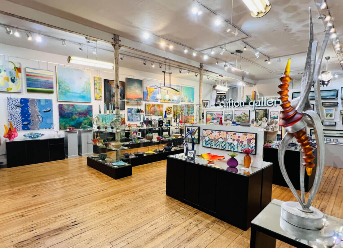 Art gallery interior with wooden floors, showcasing colorful paintings and sculptures under bright lights—a vibrant art exhibition inspired by Memphis galleries and the upcoming Art by Design 2026.
