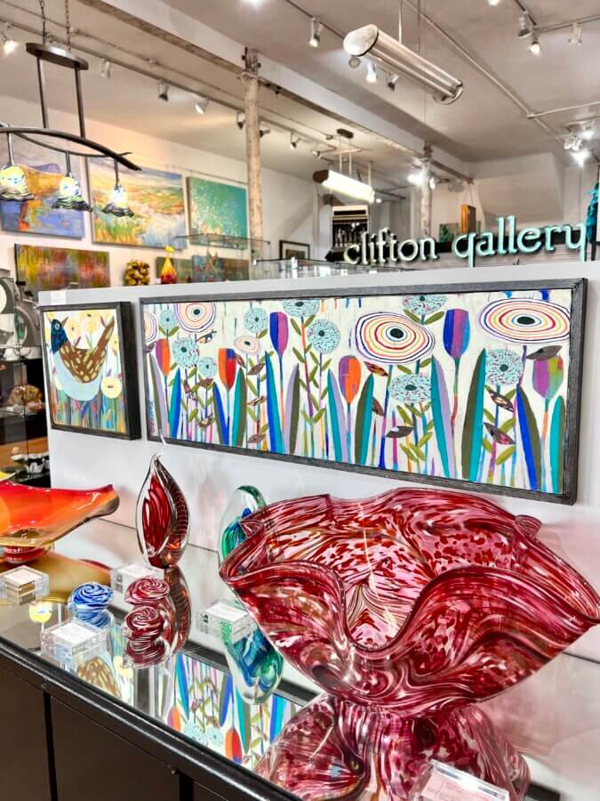 7 Memphis Galleries Exhibiting at Art by Design 2026 - 6 Glass art pieces and colorful abstract paintings exhibiting on shelves and walls in a well-lit Memphis Galleries space as part of Art by Design 2026.