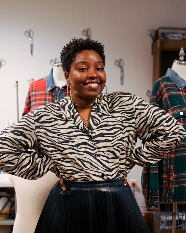 She's Changing the Way Memphis Thinks About Clothing - 7 Cari Harris stands with hands on hips, smiling in a zebra print top and black skirt. Mannequins and plaid garments fill the sewing studio in the background.