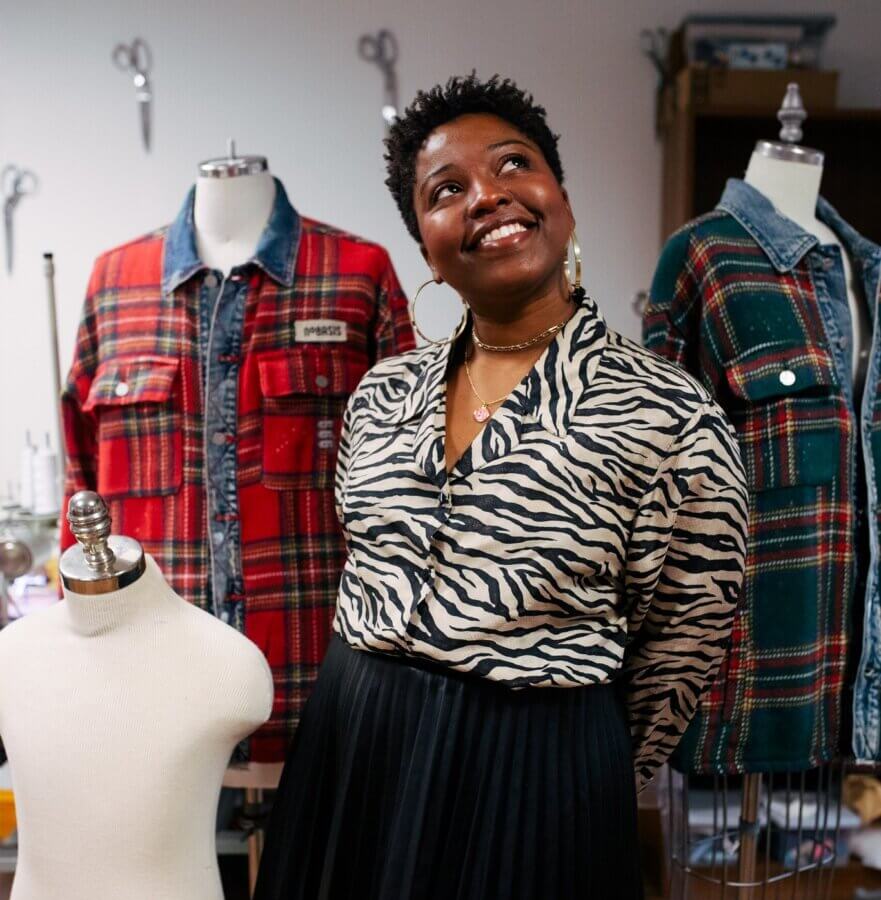 She's Changing the Way Memphis Thinks About Clothing - 2 A woman stands smiling in a workspace, surrounded by mannequins displaying plaid jackets and a white dress form.