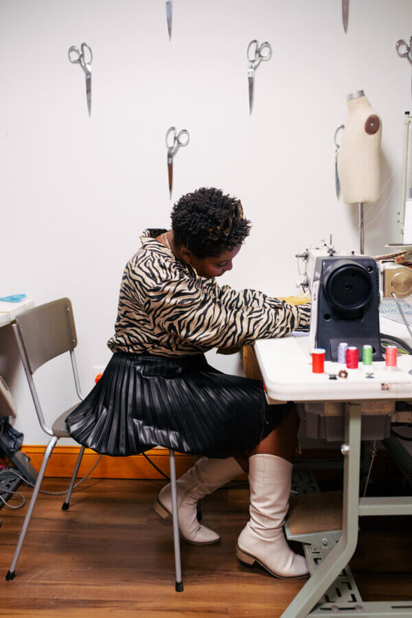 She's Changing the Way Memphis Thinks About Clothing - 4 A person sits at a sewing machine in a workspace, surrounded by scissors on the wall and sewing supplies on the table.