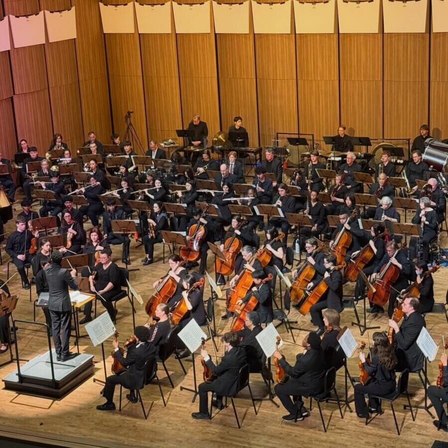 Meet the Local Flutist Behind the Memphis Youth Symphony Program - 4 A symphony orchestra performs on stage, with musicians playing string, woodwind, brass, and percussion instruments while a conductor leads them.