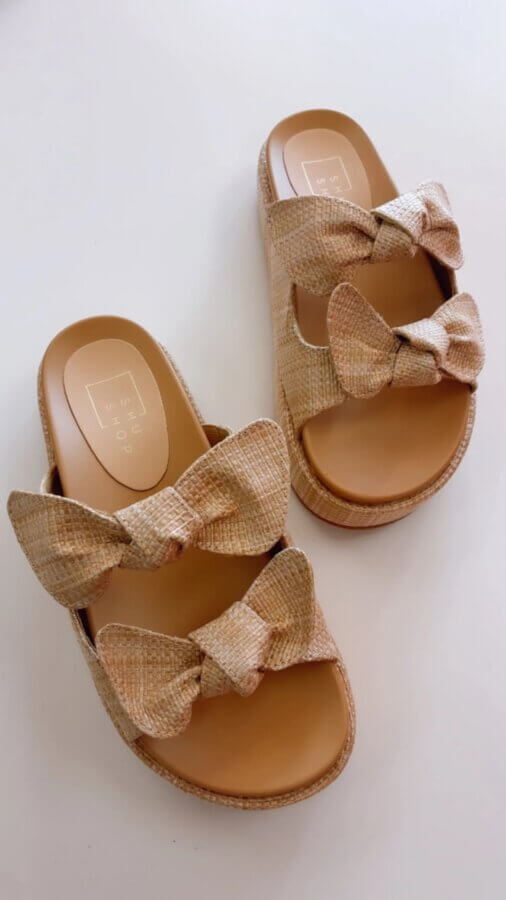 15 Memphis FINDS at Local Shops: Spring Dresses, Home Decor & More! - 5 A pair of tan slide sandals with two large woven bows on each strap, featured in the Memphis FINDS March collection and placed on a white background.