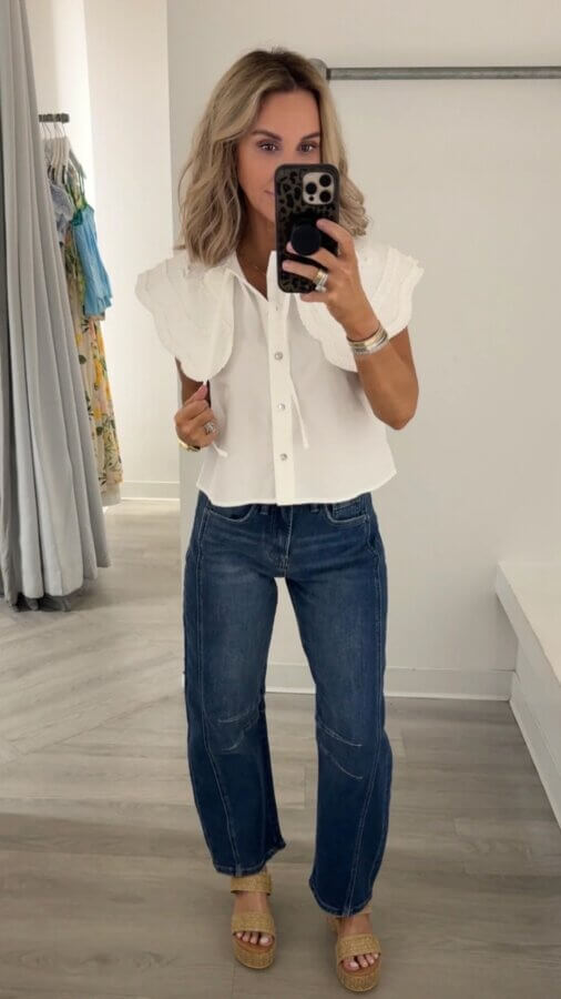 15 Memphis FINDS at Local Shops: Spring Dresses, Home Decor & More! - 6 Woman takes a mirror selfie wearing a white short-sleeve blouse, blue jeans, and wedge sandals in a minimalist fitting room, showcasing her latest Memphis FINDS from March.