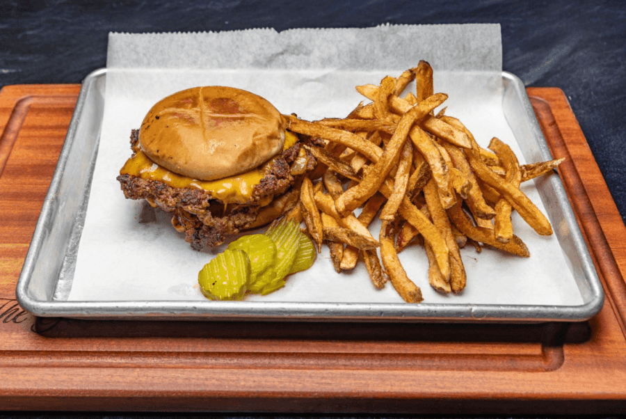 7 Must-Try Memphis Smashburgers - 7 A must-try cheeseburger with a toasted bun, melted cheese, and two pickles is served alongside crispy French fries on a metal tray lined with parchmentโone of the best smash burgers in Memphis.