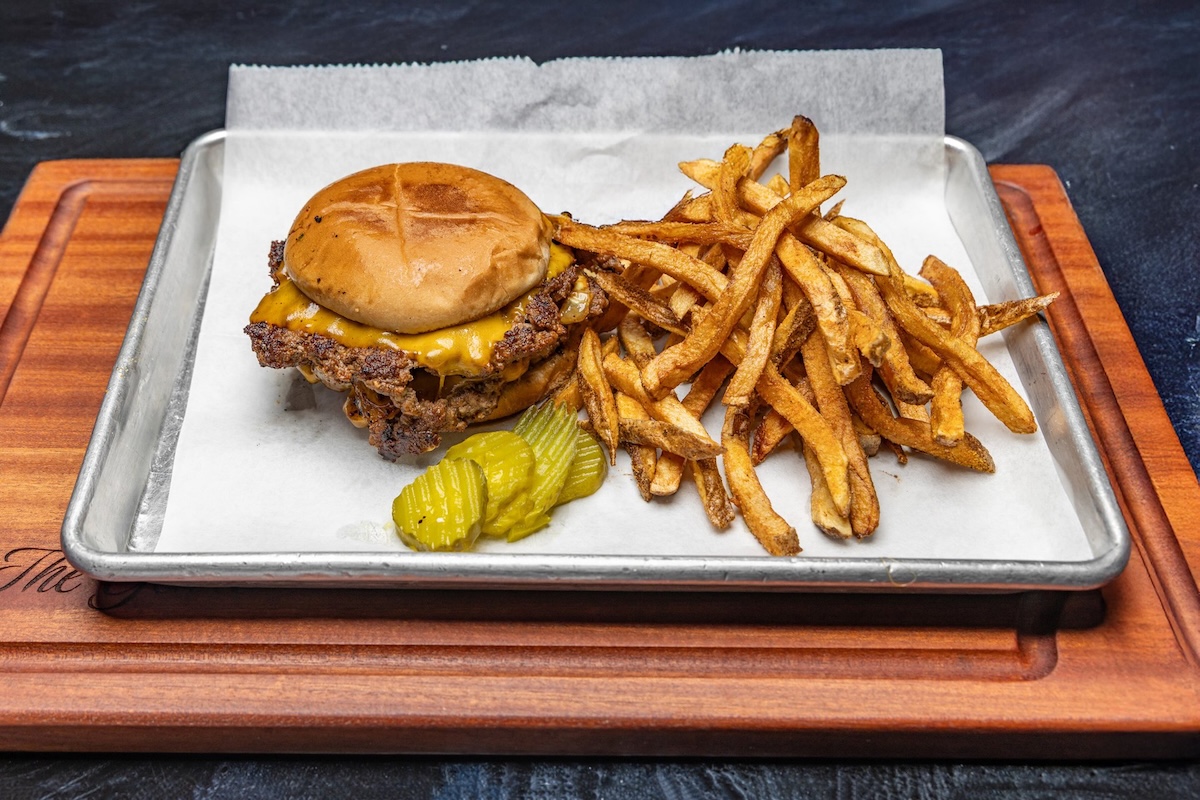 A Memphis must-try: a smash burger with pickles and a side of crispy French fries, all served on a metal tray lined with parchment paper.